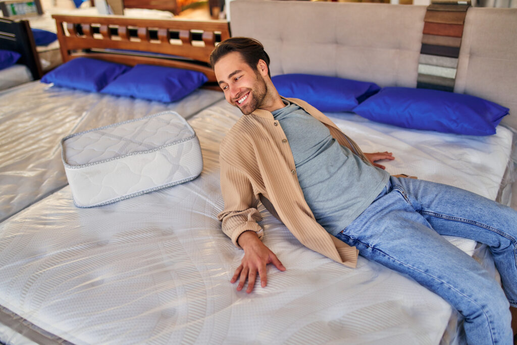 The young man lay down on the bed, trying the mattress for softness in the store. Buying a bed and bedding.