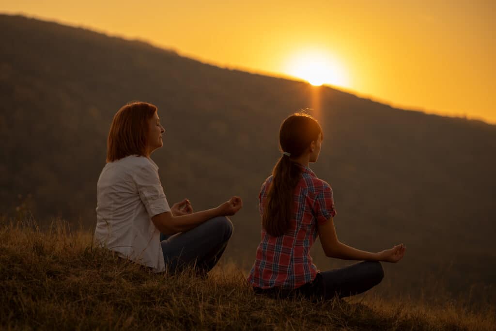 Two people meditating in the mountains with the sunrise