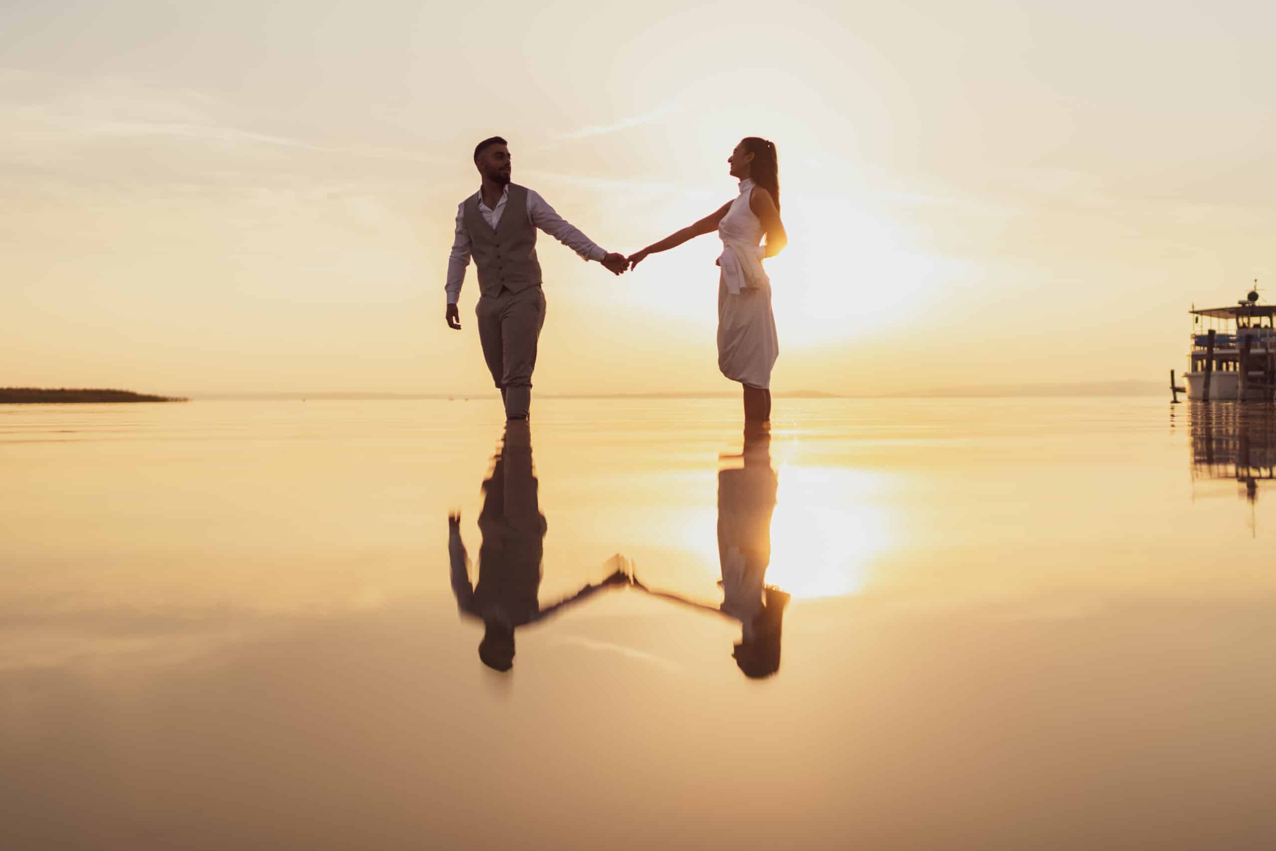 Loving couple enjoying sunset and standing in the shallow lake with sunset