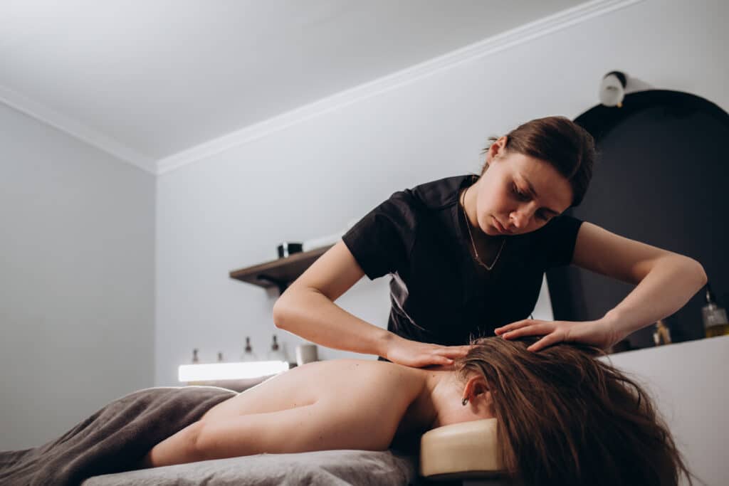 Portrait of a professional female masseuse doing therapeutic massage to her client at the clinic. Concept of relax and body care