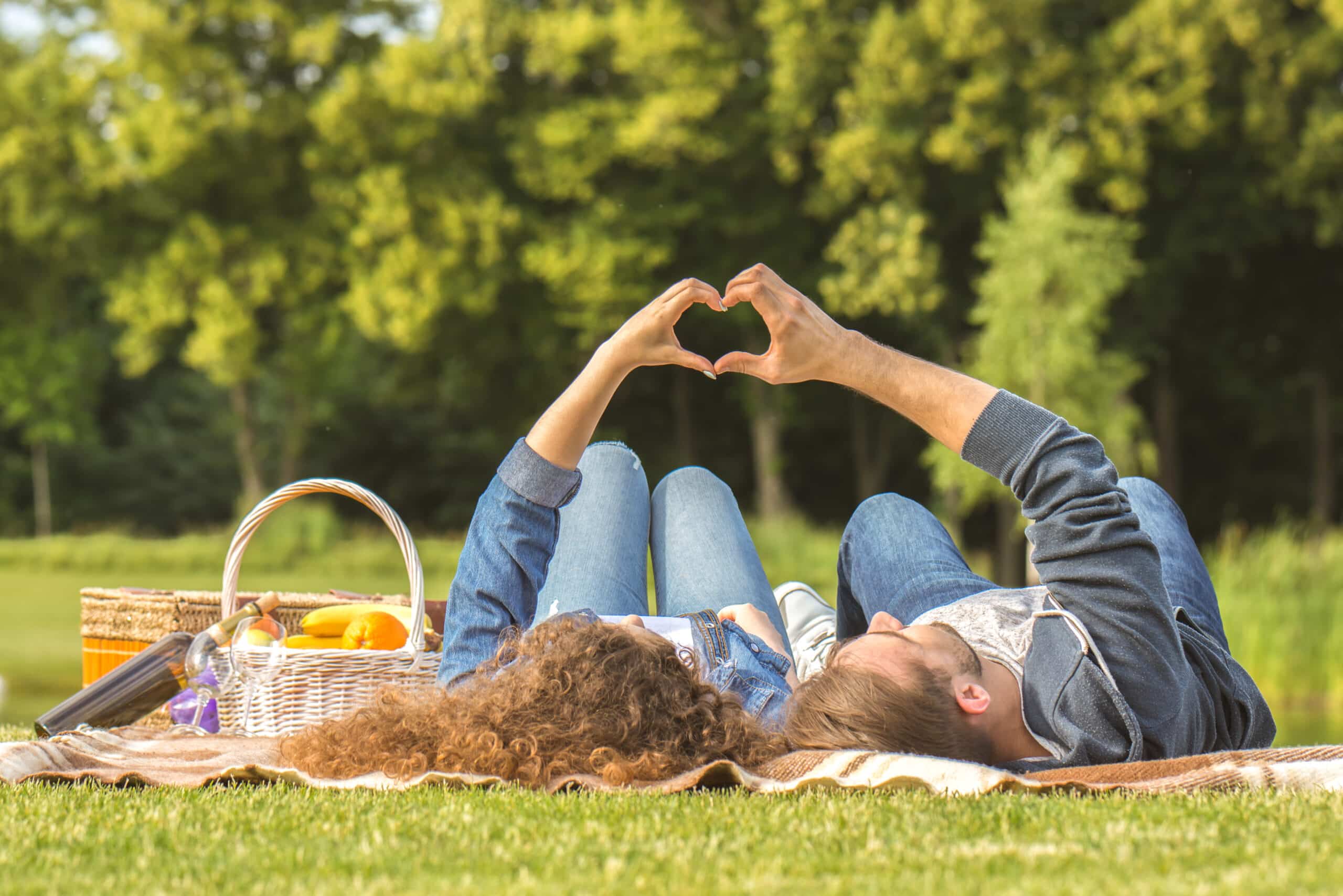 The man and woman lying on the grass and gesturing love symbol
