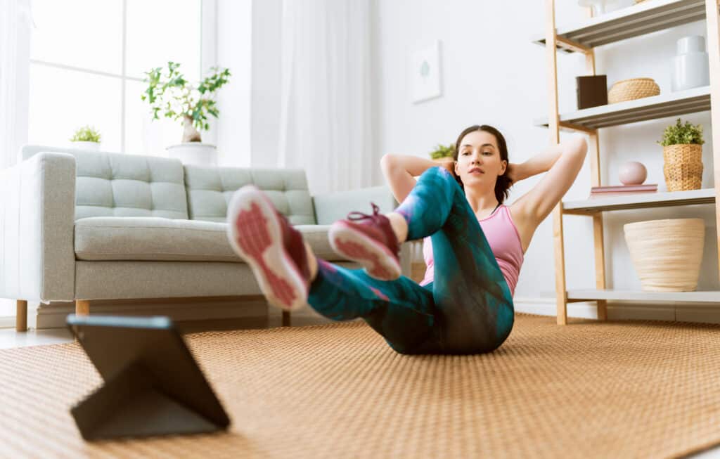 Young woman in activewear watching online courses on tablet while exercising at home