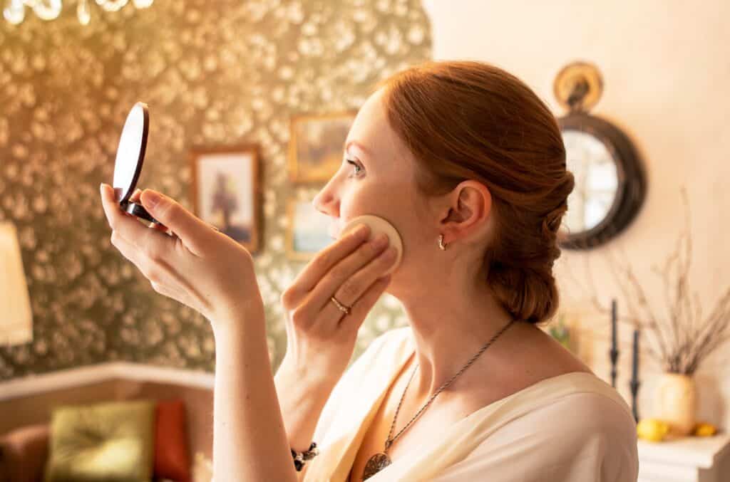 Young girl powdering her face in front of a mirror